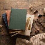 Best gifts for book lovers — a stack of books with a gold bookmark, reading glasses and a reading light