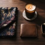 Best luxury gifts — a silk scarf, lit candle, leather wallet and gold jewelry box arranged elegantly