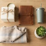 Best gifts under $50 — a candle gift box, leather notebook, tumbler, succulent and folded scarf on a light wood table